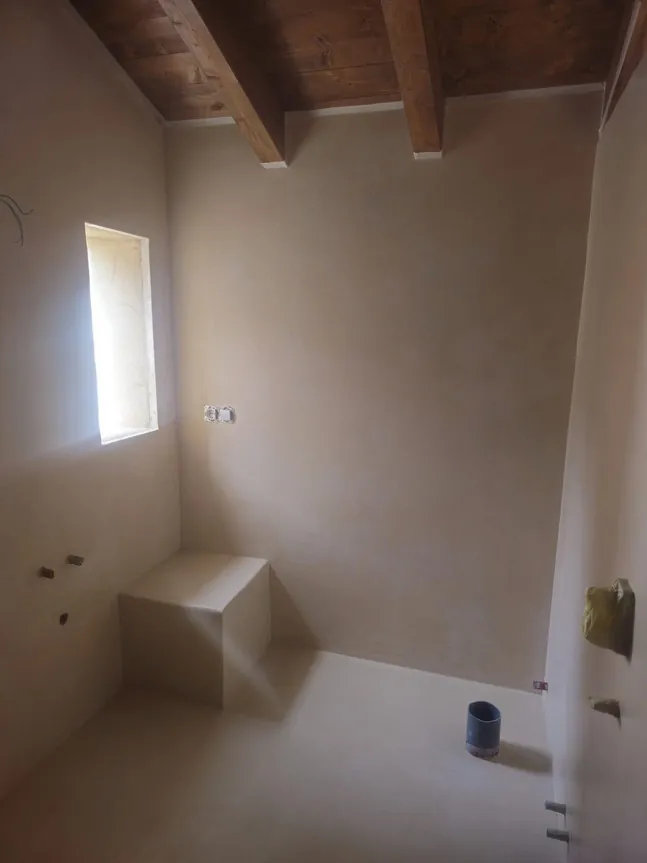 Ducha de obra con banco, vigas de madera y paredes en Estukum